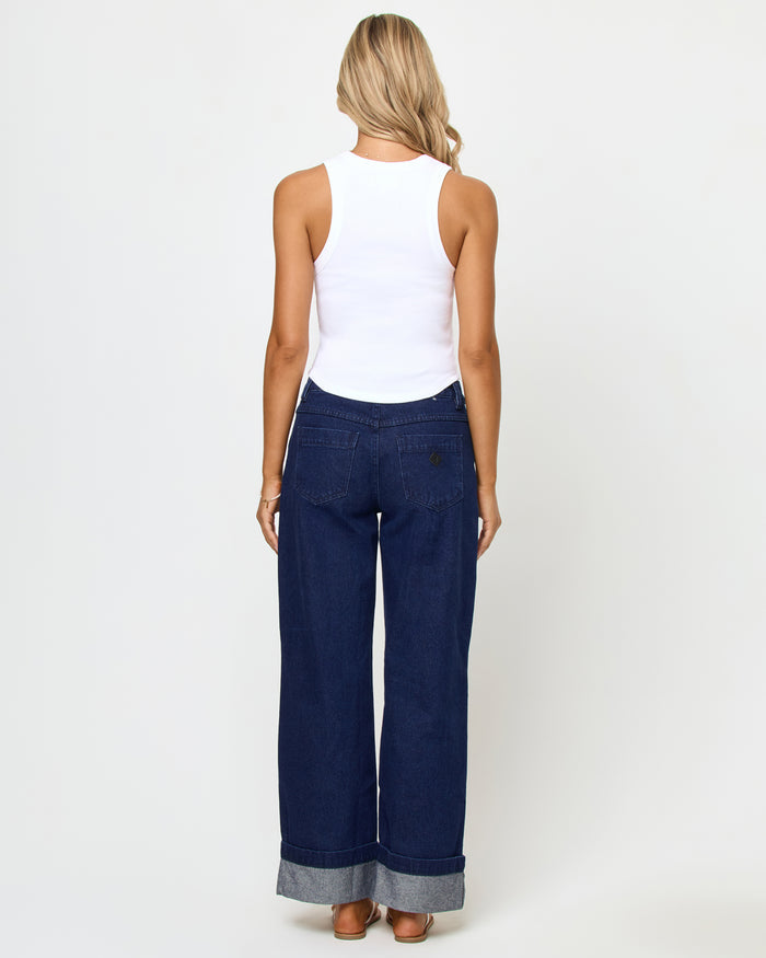 Back view of a model wearing the LSPACE Ash Tank in oysters, showing the racerback detail of the white cropped ribbed tank, styled with dark navy wide-leg cuffed jeans.