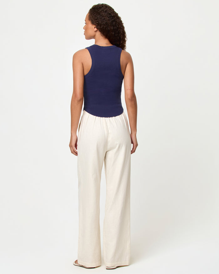 Back view of a model wearing the LSPACE Ash Tank in sardine, showing the racerback detail of the navy blue cropped ribbed tank, styled with cream wide-leg pants.