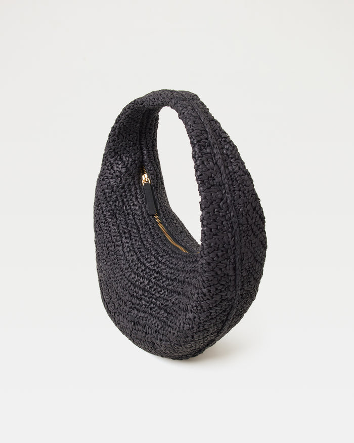Angled view of the Aya Bag in black showing the woven raffia texture and gold zipper closure.