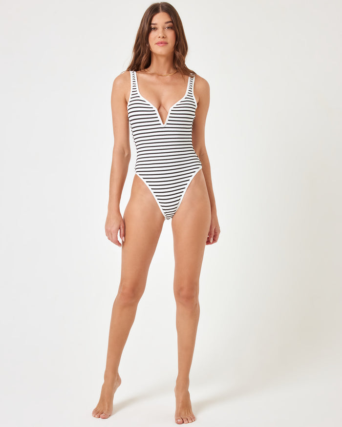 Full-length front view of a model wearing the LSPACE Sail Along Stripe Coco One Piece Swimsuit, showcasing the plunging V-neckline and high-cut leg of the navy and white striped one-piece.