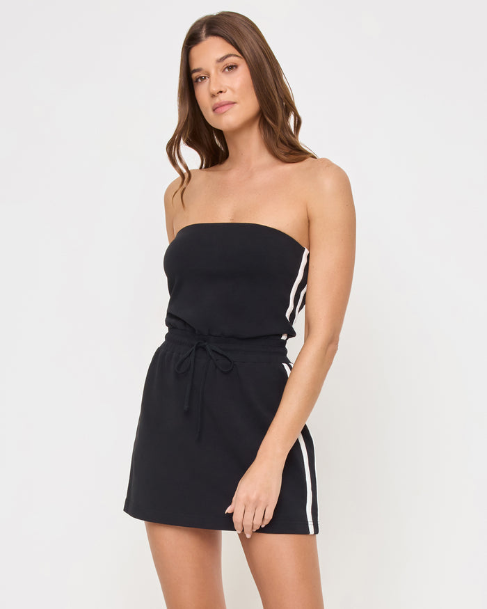 Three-quarter view of the LSPACE Decker Dress in black-cream on a model against a light background, showing the cream trim detail of the active mini dress.