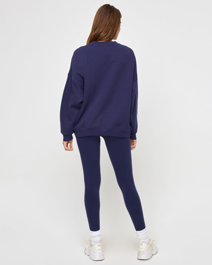 Back view of a model wearing the LSPACE Legend Sweatshirt in midnight blue, showing the oversized silhouette and solid navy back, styled with matching navy leggings.