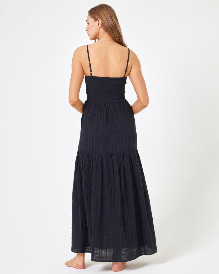 Back view of a model wearing the LSPACE Mallorca Dress in black, showing the adjustable spaghetti straps and smocked back of the tiered maxi dress.