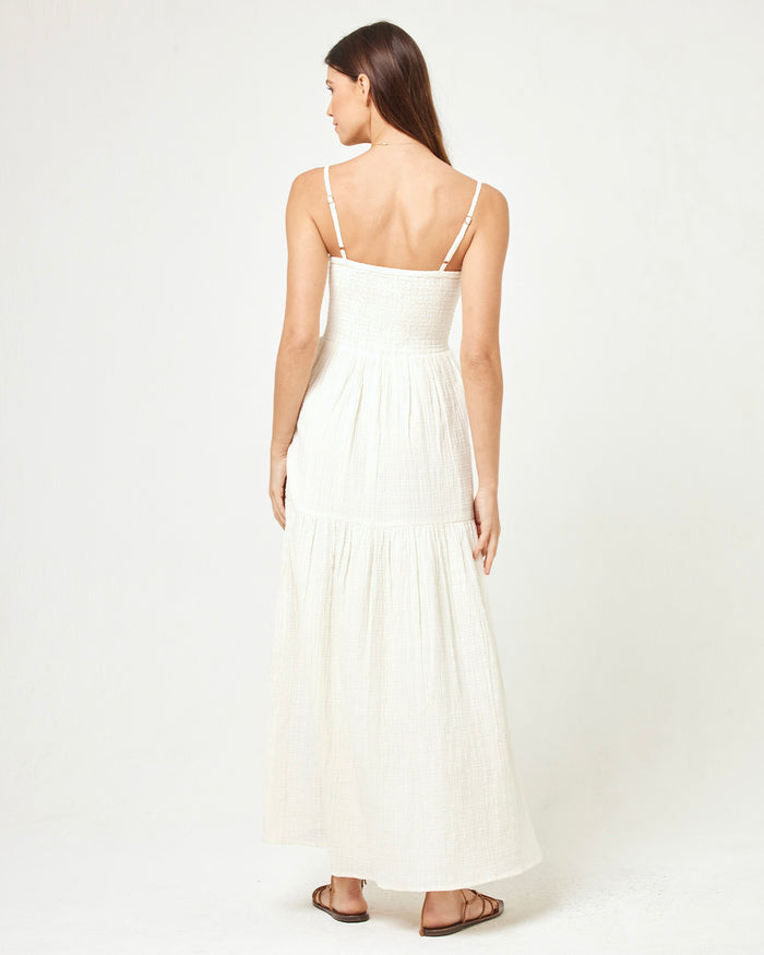 Back view of a model wearing the LSPACE Mallorca Dress in cream, showing the adjustable spaghetti straps and smocked back of the tiered cream maxi dress.
