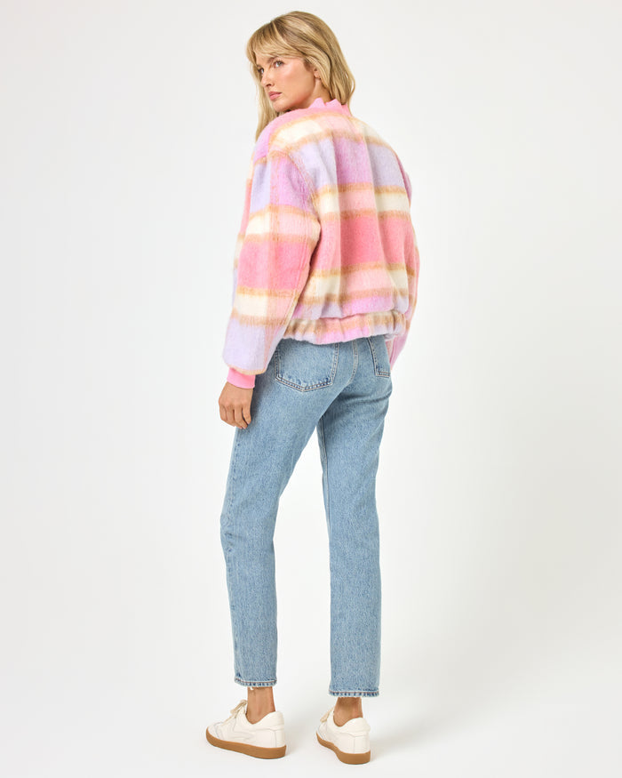 Back view of a model wearing the LSPACE Quinn Jacket in point dume plaid, showing the pink, lavender, and cream fuzzy plaid pattern across the bomber jacket back, styled with wide-leg jeans.