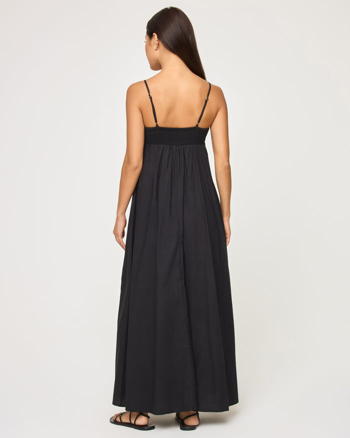 Back view of a model wearing the LSPACE Raveena Dress in black, showing the adjustable spaghetti straps, smocked back bodice, and full flowing maxi skirt.