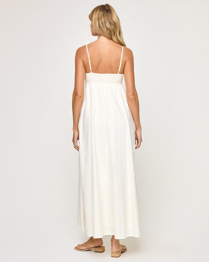 Back view of a model wearing the LSPACE Raveena Dress in cream, showing the adjustable spaghetti straps, low back with a smocked waistband, and full flowing maxi skirt.