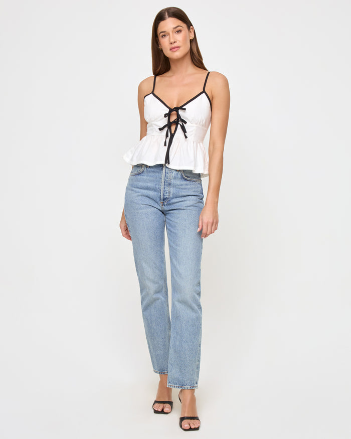 Front view of a model wearing the LSPACE Agnes Top in cream-black, a peplum camisole with black contrast tie straps and a flared peplum hem, styled with wide-leg jeans.