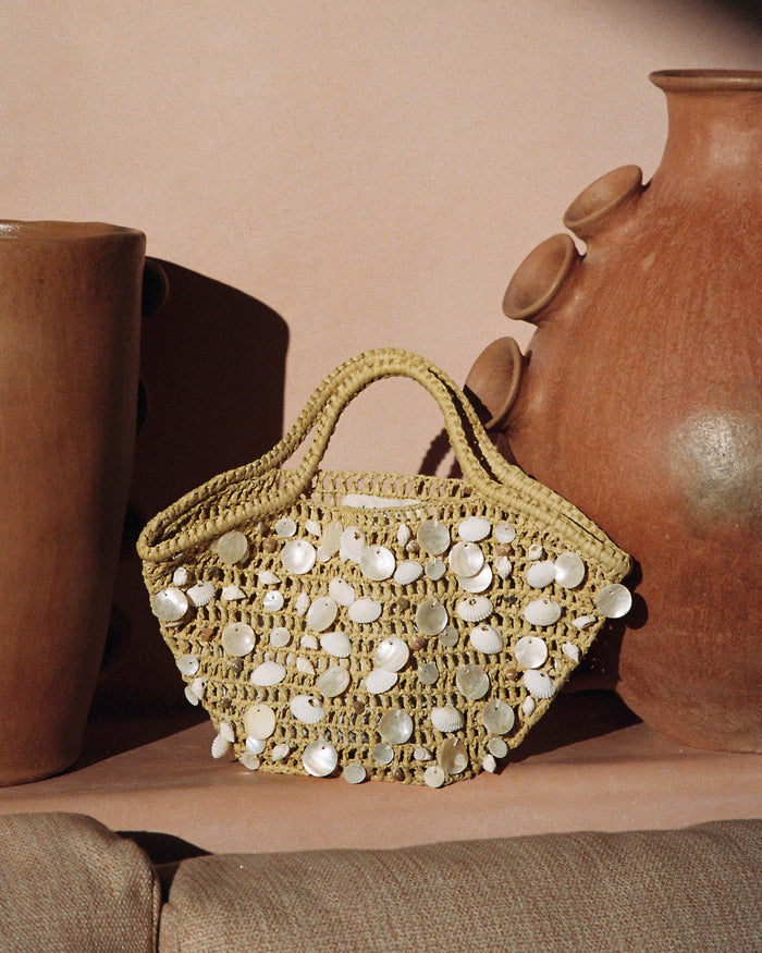 Lifestyle image of the cream and natural Alba Bag resting on a surface beside ceramic pots.