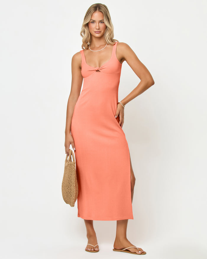 Front view of a model wearing the LSPACE Alexis Dress in fresh squeezed, a fitted ribbed midi dress in peach with thick straps, a sweetheart neckline, front knot detail, and side slit.
