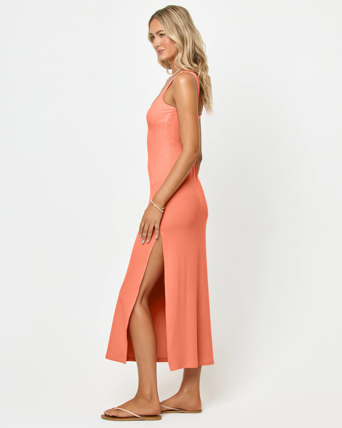 Side view of a model wearing the LSPACE Alexis Dress in fresh squeezed, showing the fitted silhouette and open side slit of the peach ribbed midi dress.