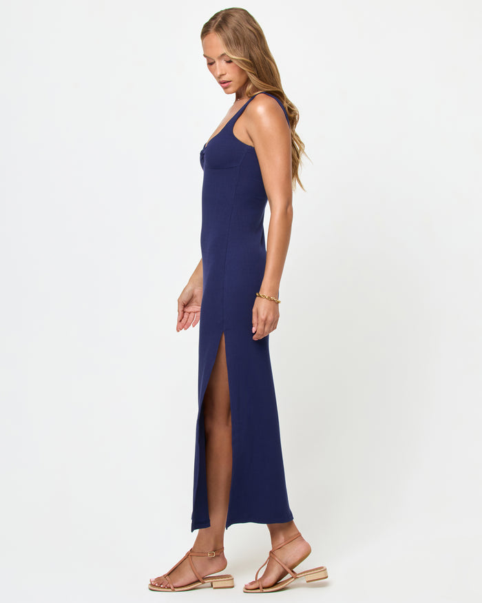 Side view of a model wearing the LSPACE Alexis Dress in midnight blue, showing the fitted silhouette and side slit of the navy ribbed midi dress.