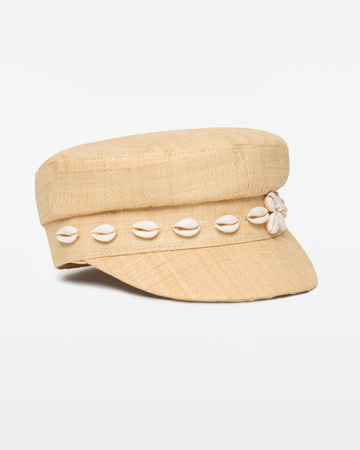 Off-model side view of the Alfama Cap in natural, a woven raffia baker boy cap with a cowrie shell band trim, on a white background.