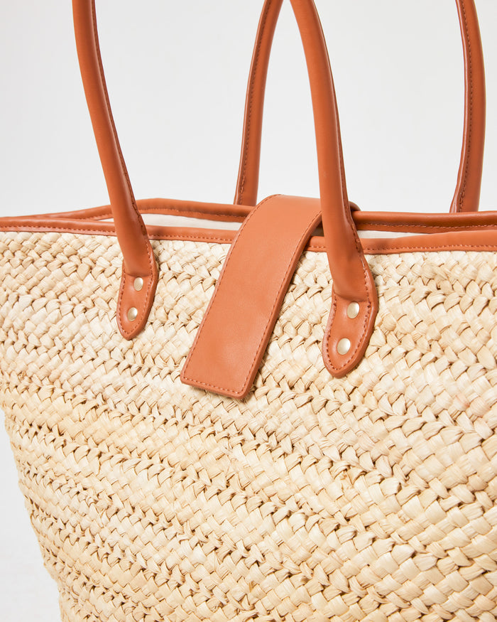 Close-up of the Alfie Bag in natural showing the woven straw texture and brown leather handle hardware.