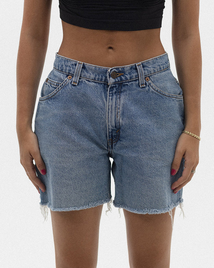 Front detail view of a model wearing the aligrace Long Baggy Short in light wash, showing the relaxed-fit denim shorts with a raw hem, styled with a black crop top.