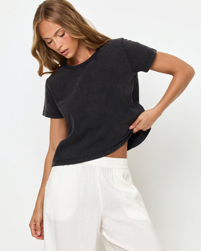 Angled front view from above of a model wearing the LSPACE All Day Top in black, styled with white wide-leg track pants with a black side stripe.