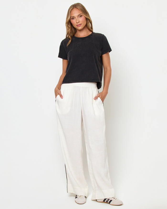 Full body front view of a model wearing the LSPACE All Day Top in black, styled with white wide-leg track pants and sneakers.