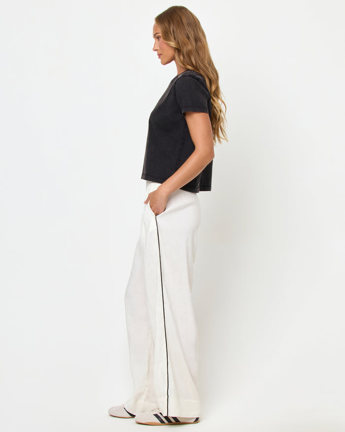 Side view of a model wearing the LSPACE All Day Top in black, styled with white wide-leg track pants.