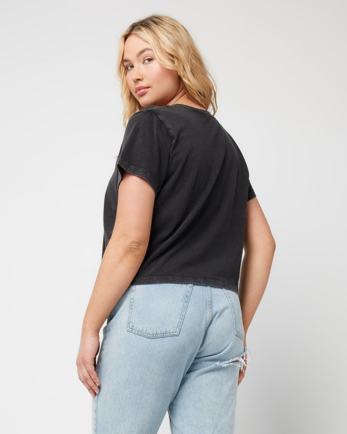 Angled back view of a model looking over her shoulder wearing the LSPACE All Day Top in black, styled with light wash jeans.