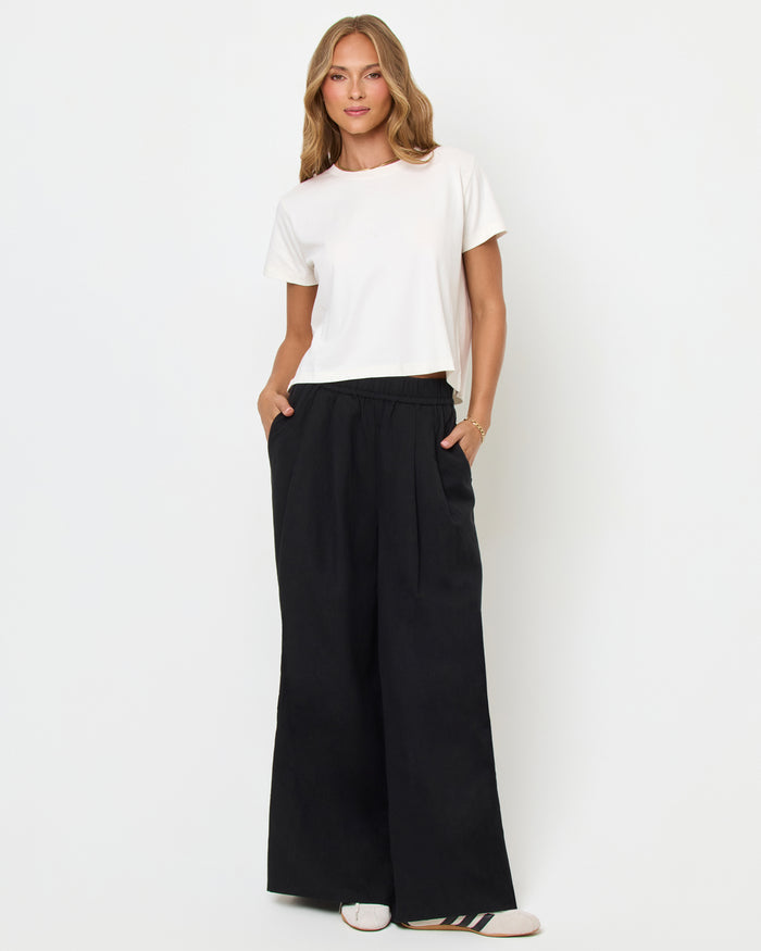 Full body front view of a model wearing the LSPACE All Day Top in cream, styled with black wide-leg pants with a cream side stripe and sneakers.