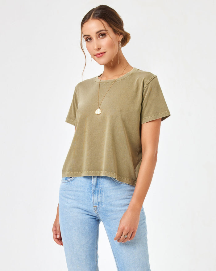 Front view of a smiling model wearing the LSPACE All Day Top in olive branch, styled with light wash jeans.