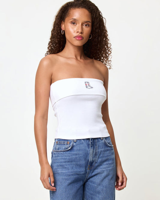 Front view of a model wearing the LSPACE Andie Top in yallspace, a white ribbed strapless tube top with a fold-over edge and embroidered cowboy boot graphic, styled with medium wash blue jeans.