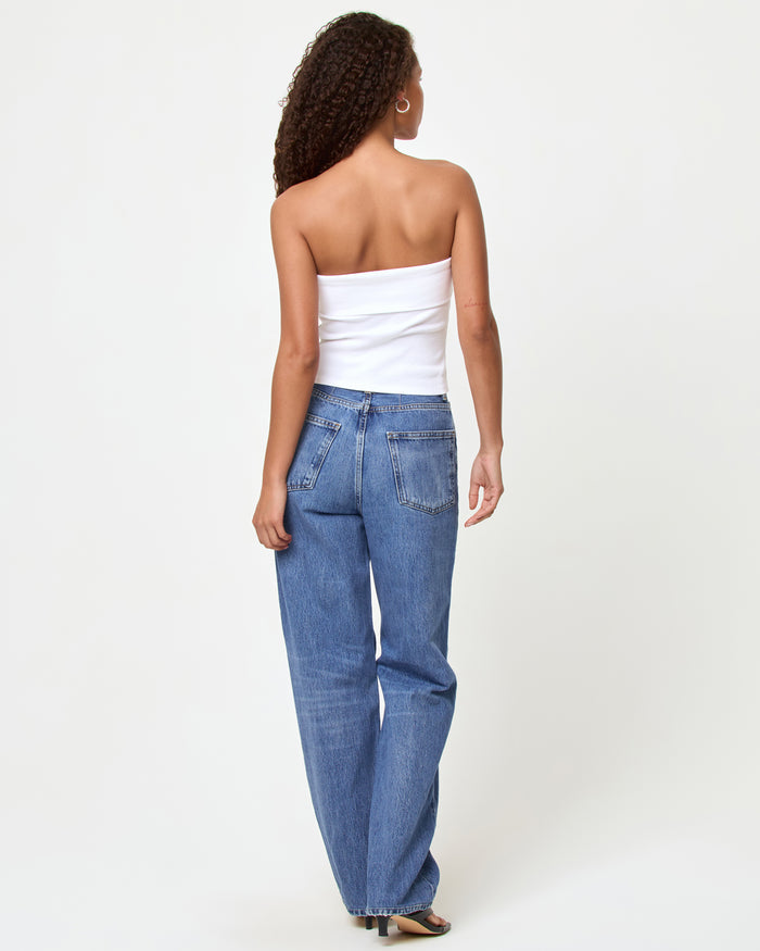 Back view of a model wearing the LSPACE Andie Top in yallspace, showing the back of the white ribbed strapless tube top, styled with medium wash wide-leg jeans and black heeled sandals.