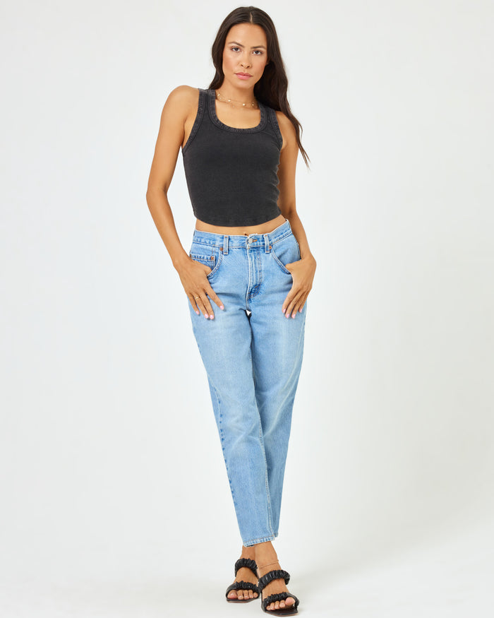 Full body front view of a model wearing the LSPACE Ash Tank in black, a ribbed racerback crop tank, styled with light wash jeans and black sandals.
