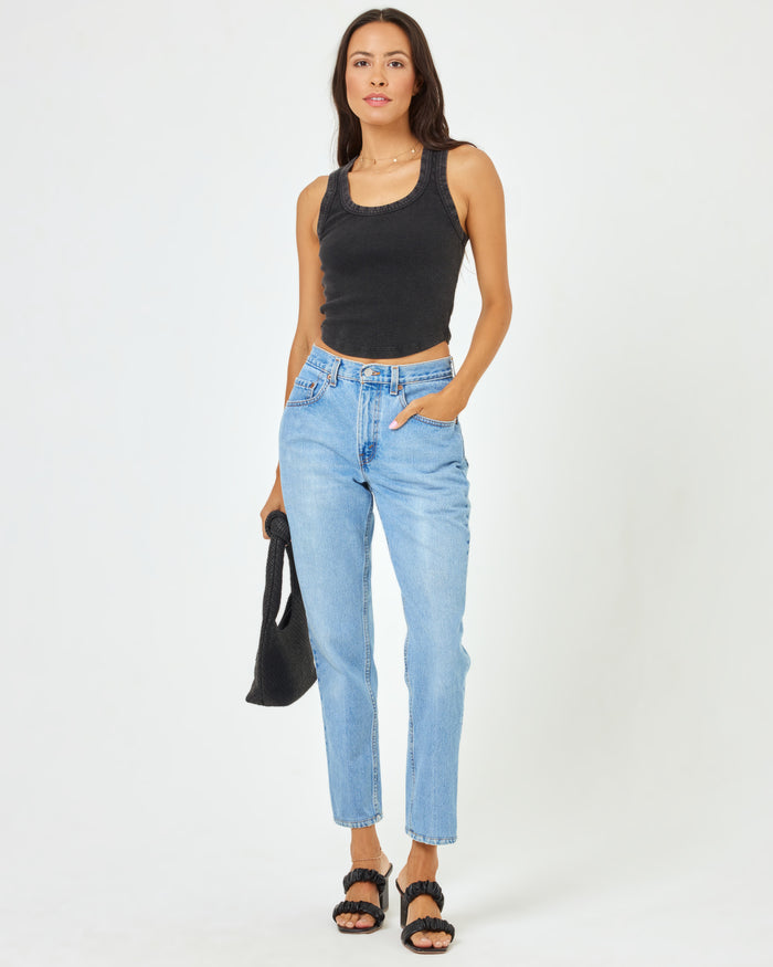 Full body front view of a model wearing the LSPACE Ash Tank in black, a ribbed racerback crop tank, styled with light wash jeans, black sandals, and carrying a black bag.