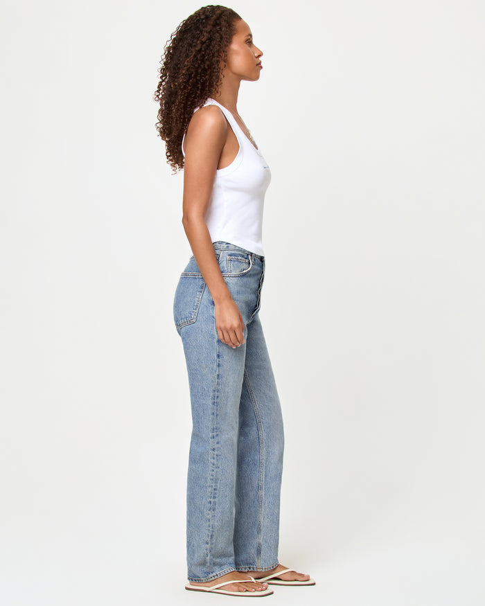 Side view of a model wearing the LSPACE Ash Tank in happier in a bikini, a white cropped ribbed racerback tank, styled with light wash straight-leg jeans and sandals.