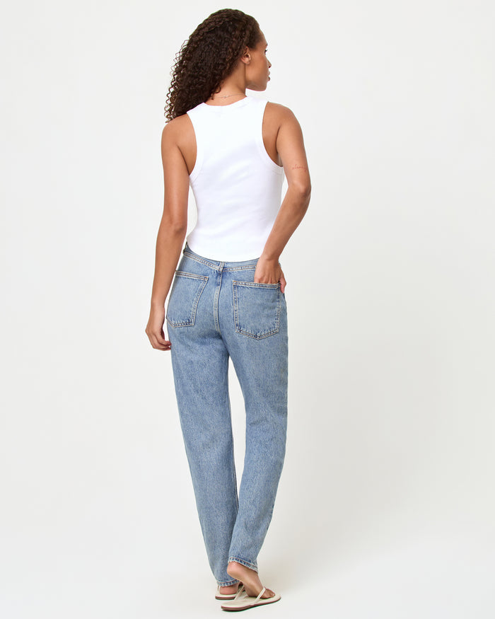 Back view of a model wearing the LSPACE Ash Tank in happier in a bikini, showing the racerback detail of the white cropped ribbed tank, styled with light wash straight-leg jeans and sandals.