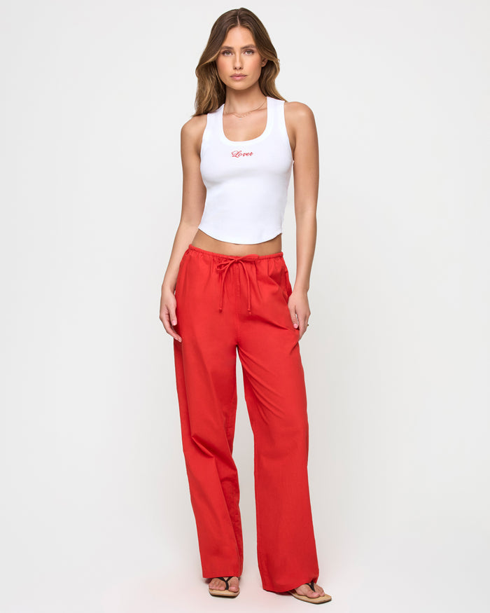 Front view of a model wearing the LSPACE Ash Tank in lover, a white cropped ribbed racerback tank with red 'Lover' script embroidery, styled with wide-leg pants.