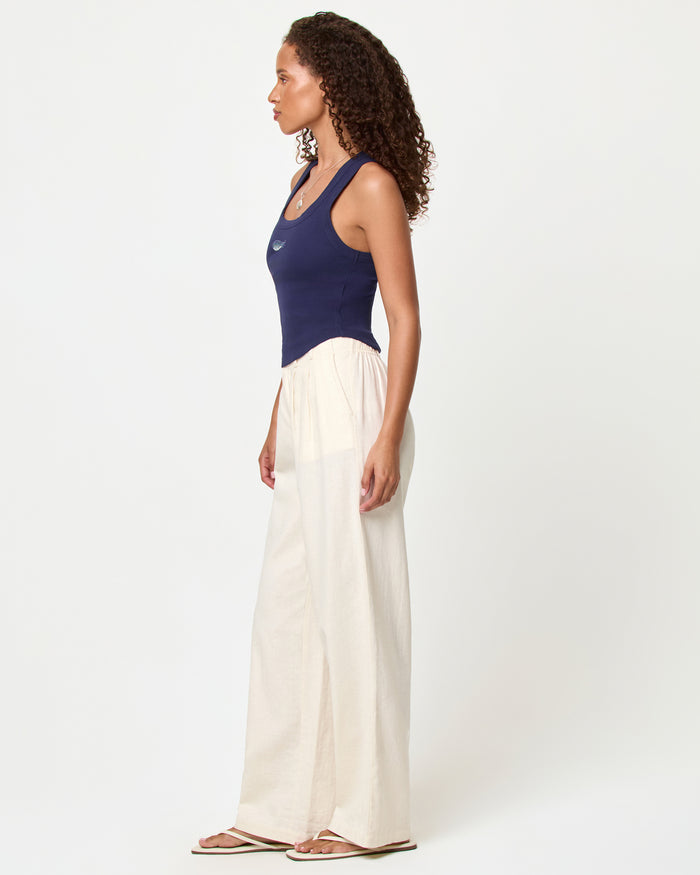 Side view of a model wearing the LSPACE Ash Tank in sardine, a navy blue cropped ribbed racerback tank, styled with cream wide-leg pants and sandals.