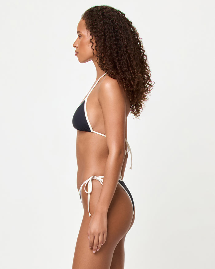Side view of a model wearing the LSPACE black-cream Levy Bikini Bottom with cream contrast trim and side-tie closure, paired with the matching Aspen Bikini Top.