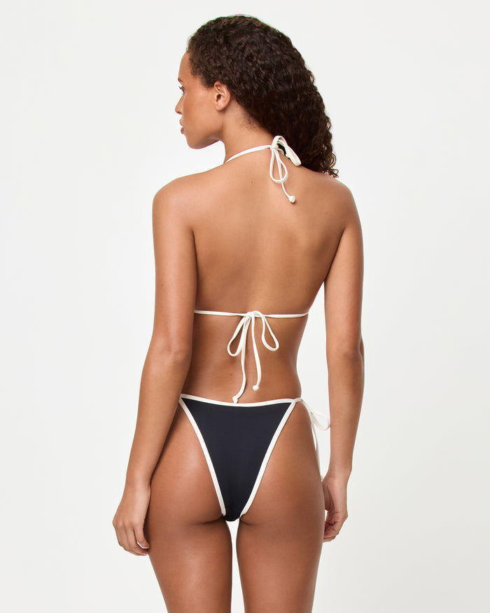 Back view of a model wearing the LSPACE black-cream Levy Bikini Bottom with cream contrast trim and side-tie closure, paired with the matching Aspen Bikini Top.