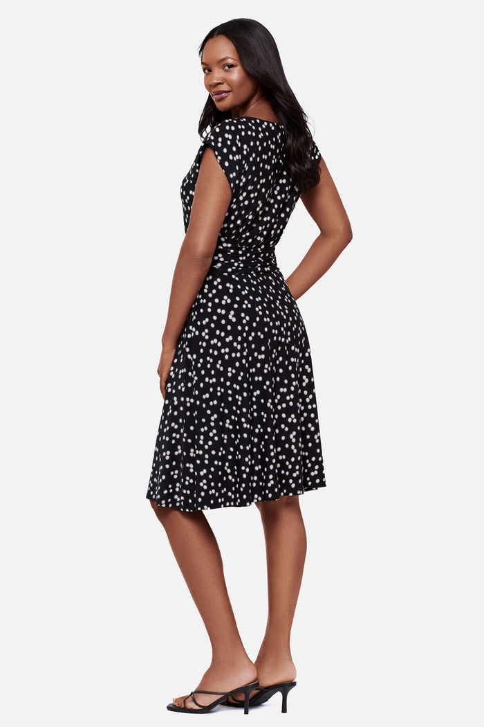 Woman faced left wearing a black and white polka dot short sleeve mid length dress