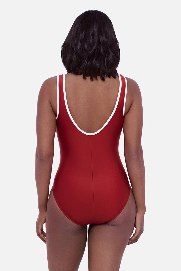 Woman turned away wearing a cherry red one-piece swimsuit with white piping on the edges