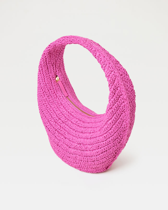 Angled view of the Aya Bag in bubblegum pink, a crescent-shaped woven raffia hobo bag, with gold zipper closure.