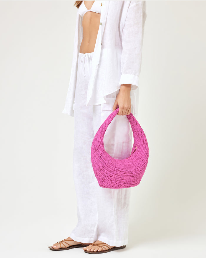 Model holding the Aya Bag in bubblegum pink at their side, paired with a white linen shirt and white wide-leg pants.