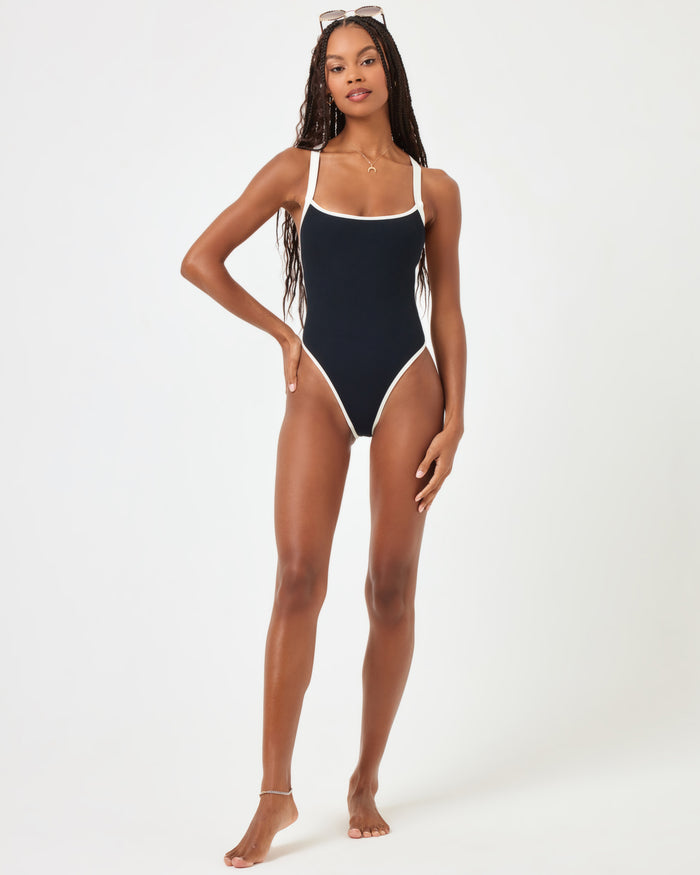 Full-length front view of a model wearing the LSPACE black-cream Baewatch One Piece Swimsuit, a ribbed style with square neckline, thin straps, cream contrast trim, and high-cut leg.