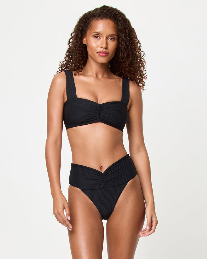 Front view of a model wearing the LSPACE black Bardot Bikini Bottom, a ribbed high-waist style with gathered center front waistband detail, paired with the black Marlee Bikini Top.