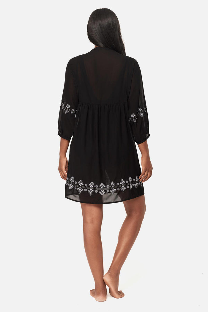 Woman turned away wearing a black beach dress swim cover up with geometric details along the edges