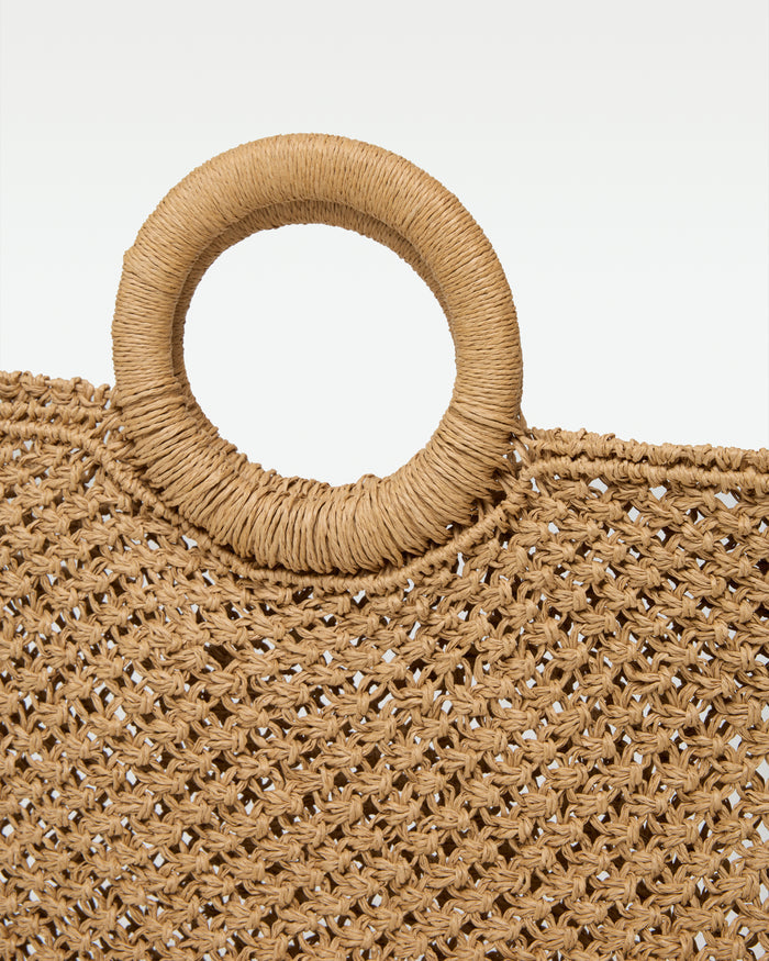 Close-up detail of the Bella Tote in natural showing the raffia-wrapped round ring handle and the open crochet weave texture.