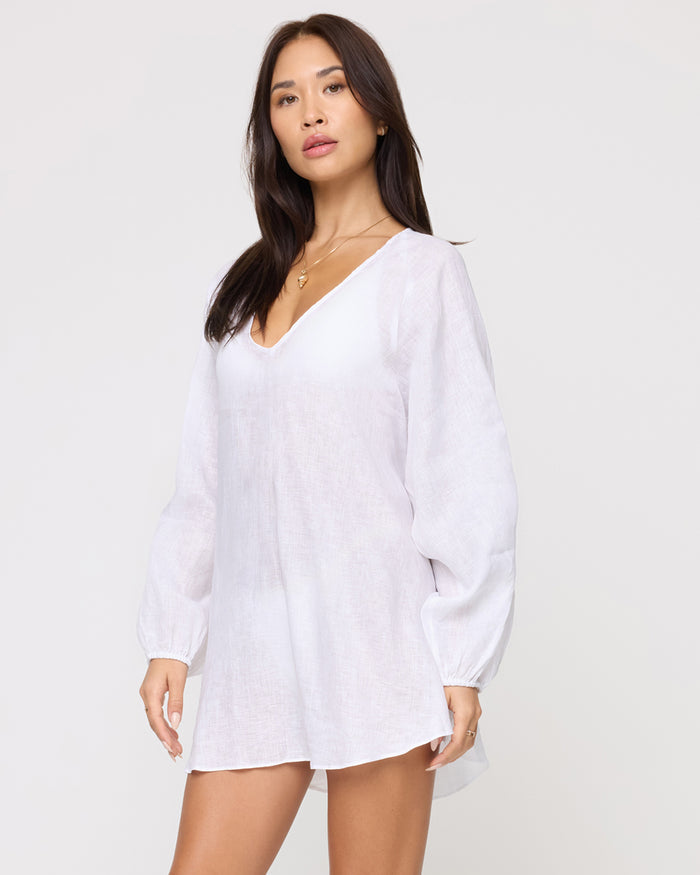 Three-quarter front view of a model wearing the LSPACE Boat Trip Tunic in white, a sheer linen mini-length tunic with a V-neckline and long balloon sleeves.