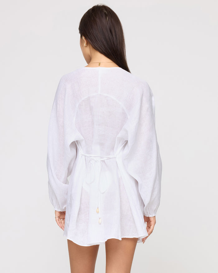 Back view of a model wearing the LSPACE Boat Trip Tunic in white, showing a circular cutout at the upper back and a tie cinched at the waist.