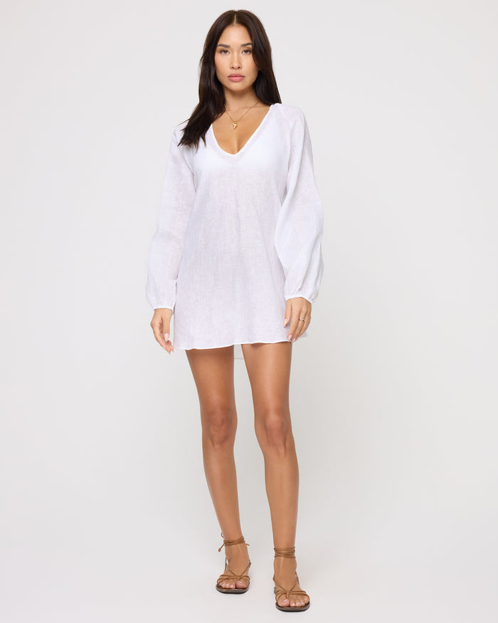 Full-length front view of a model wearing the LSPACE Boat Trip Tunic in white, a loose sheer linen tunic with a V-neckline and long balloon sleeves.