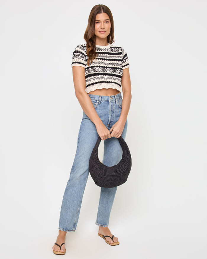 Front view of a model wearing the LSPACE Caicos Top in caicos stripe, a black-and-cream crochet stripe crop top with short sleeves and scalloped hem, styled with light-wash jeans and holding a black woven bag.
