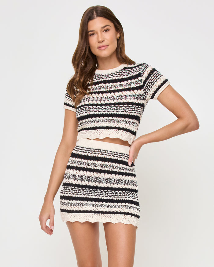 Front view of a model wearing the LSPACE Caicos Top in caicos stripe, a black-and-cream crochet stripe crop top, styled as a matching set with the Caicos Skirt with hand on hip.