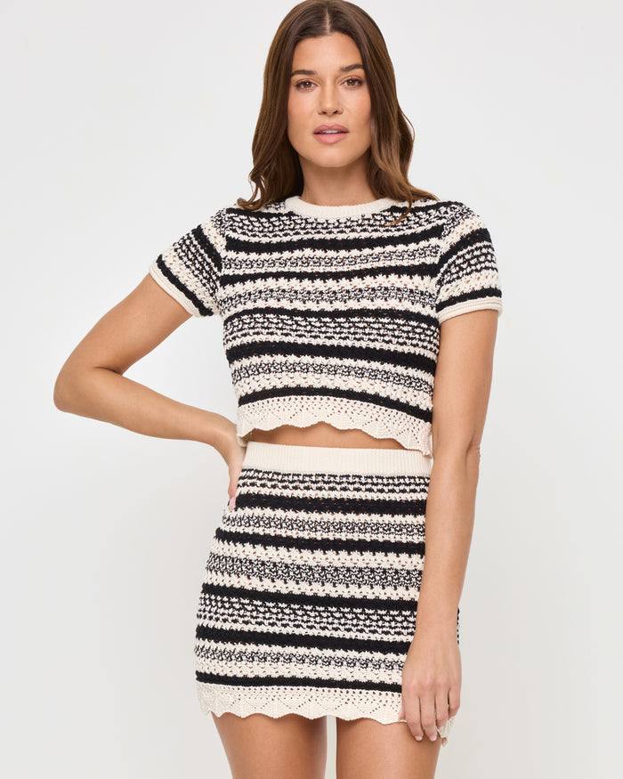 Three-quarter front view of a model wearing the LSPACE Caicos Top in caicos stripe, showing the scalloped hem and black-and-cream crochet stripe detail, styled with the matching Caicos Skirt.