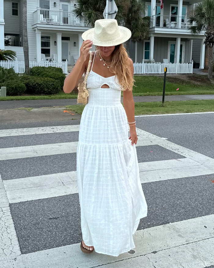 Lifestyle front view of a model wearing the LSPACE Calla Dress in cream, a tiered maxi with a bust cutout, walking outdoors, styled with a sun hat and woven bag.